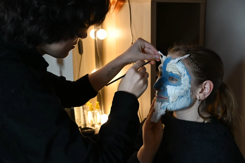 Math David Makeup applique minutieusement du maquillage bleu et blanc sur le visage d'une modèle.