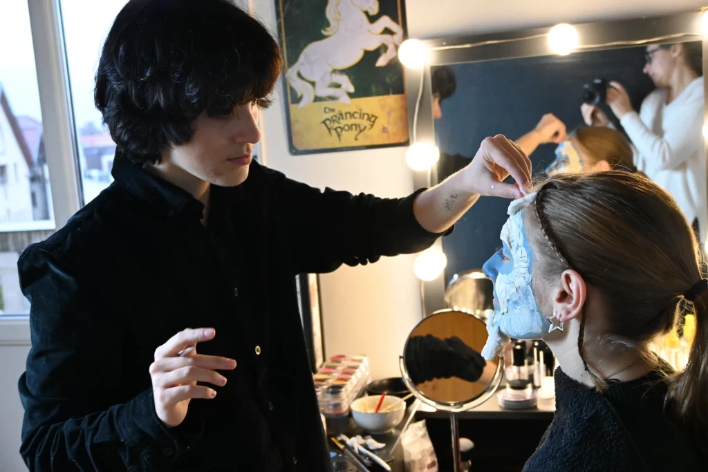 Math David Makeup applique une prothèse sur le visage d'une modèle assise, devant un miroir éclairé.