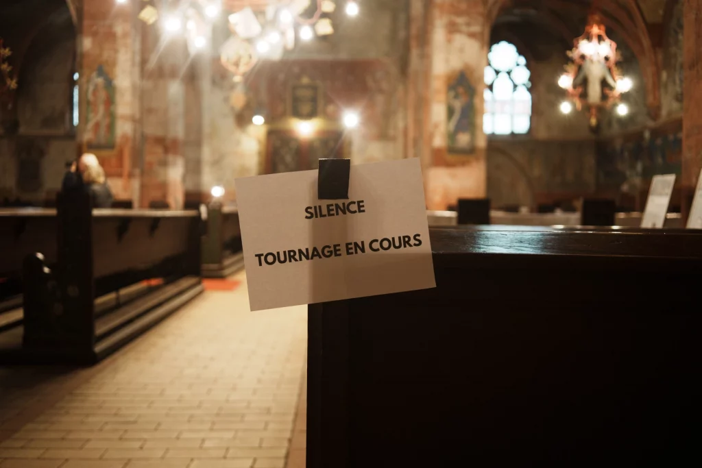 L'intérieur sombre et richement décoré d'une église, avec une pancarte accrochée à un banc indiquant « Silence, tournage en cours ».