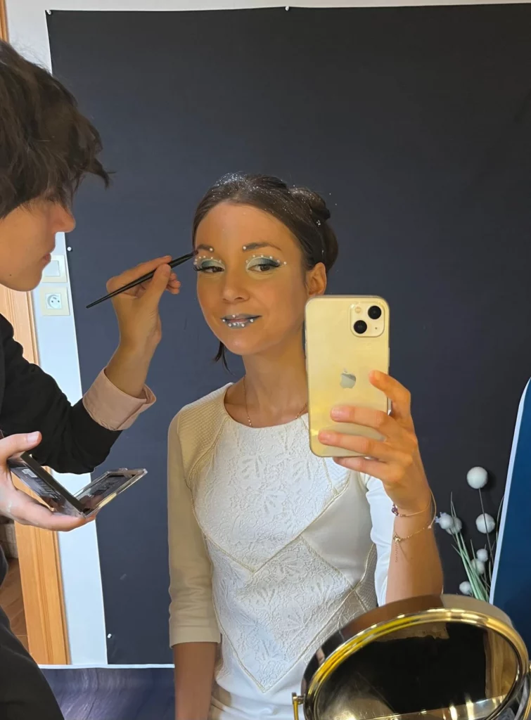 Math David Makeup en train de maquiller une modèle. Elle prend un selfie vêtue d'un haut blanc