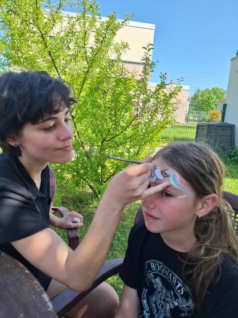 Math David Makeup peint une licorne sur le visage d'une enfant dans un décor extérieur.