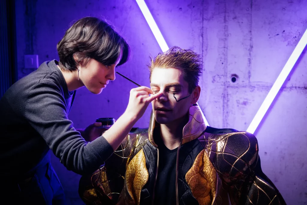 Math David Makeup de profil, en train de peindre le visage d'un homme costumé.