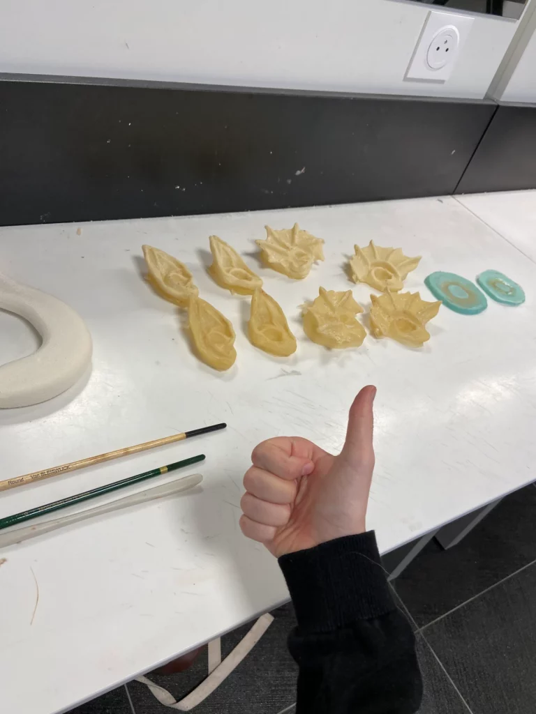 Prothèses d'oreilles jaunâtres posées sur une table blanche avec une main faisant un pouce en l'air.