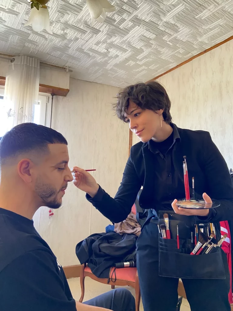 Math David Makeup debout maquillant un modèle masculin.