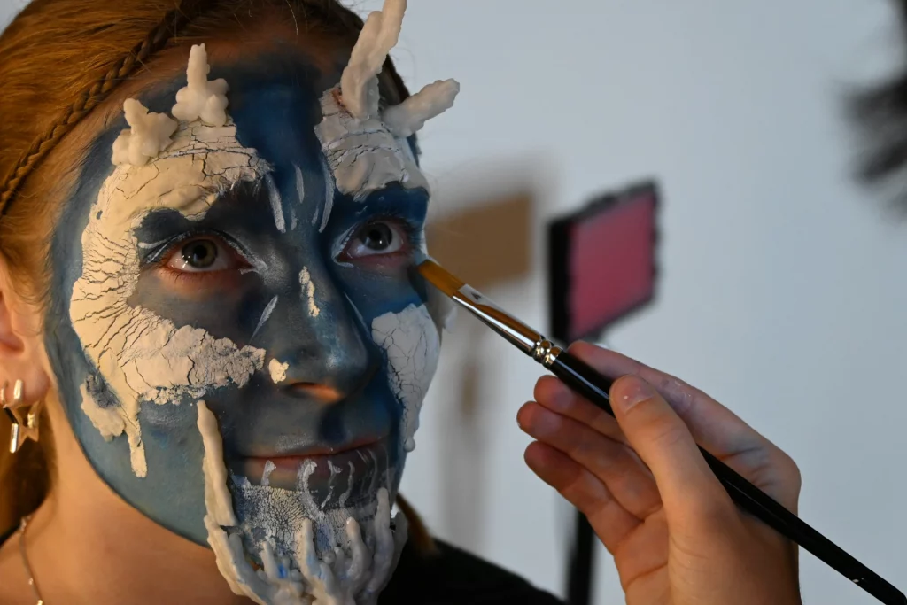 Gros plan sur le visage d'une jeune femme avec un maquillage artistique bleu et blanc.