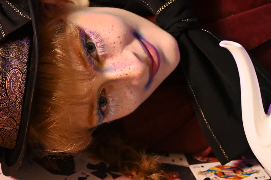 Femme au maquillage vibrant et fantaisiste, avec un fard à paupières coloré et des taches de rousseur.