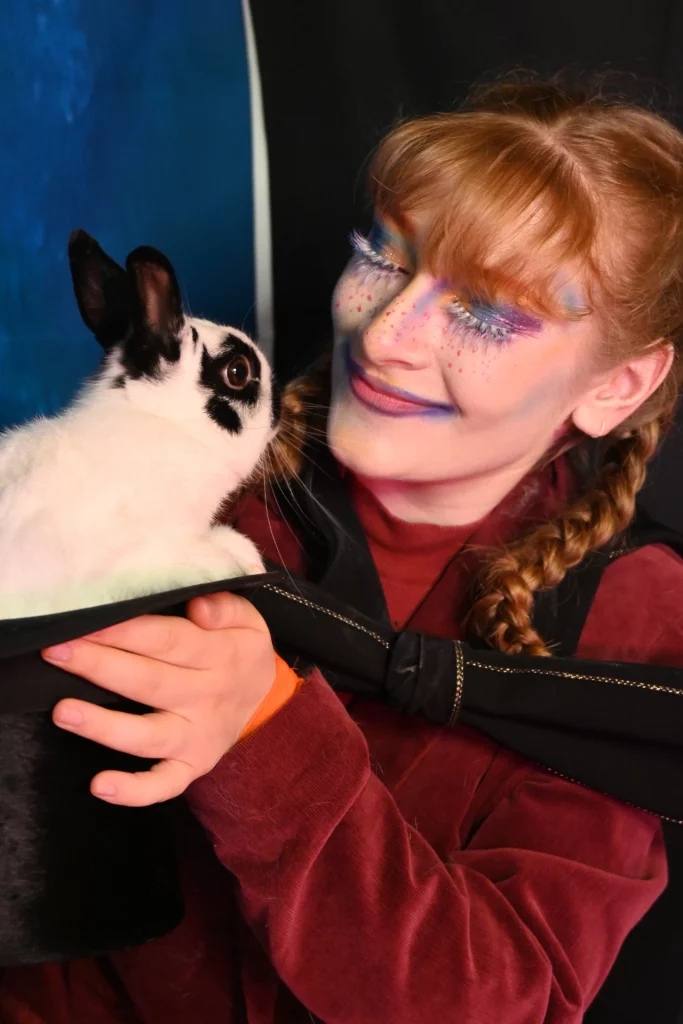 Portrait d'une femme au maquillage coloré et faux-cils tenant un lapin blanc et noir dans ses mains.