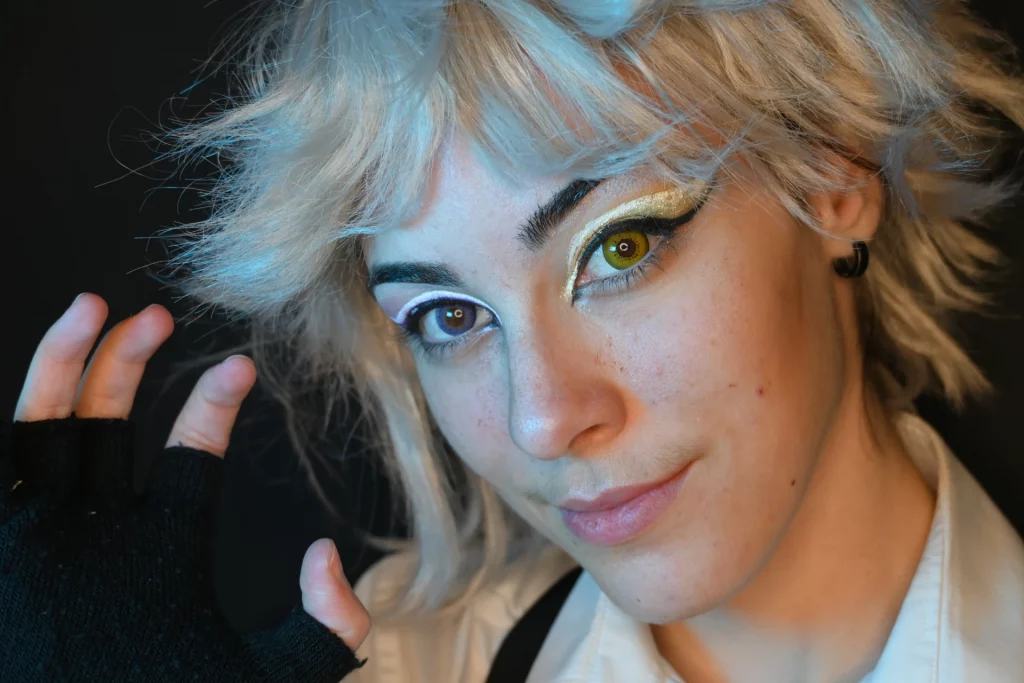 Jeune femme aux cheveux blonds courts et ébouriffés, maquillage doré saisissant autour des yeux avec un eyeliner noir.