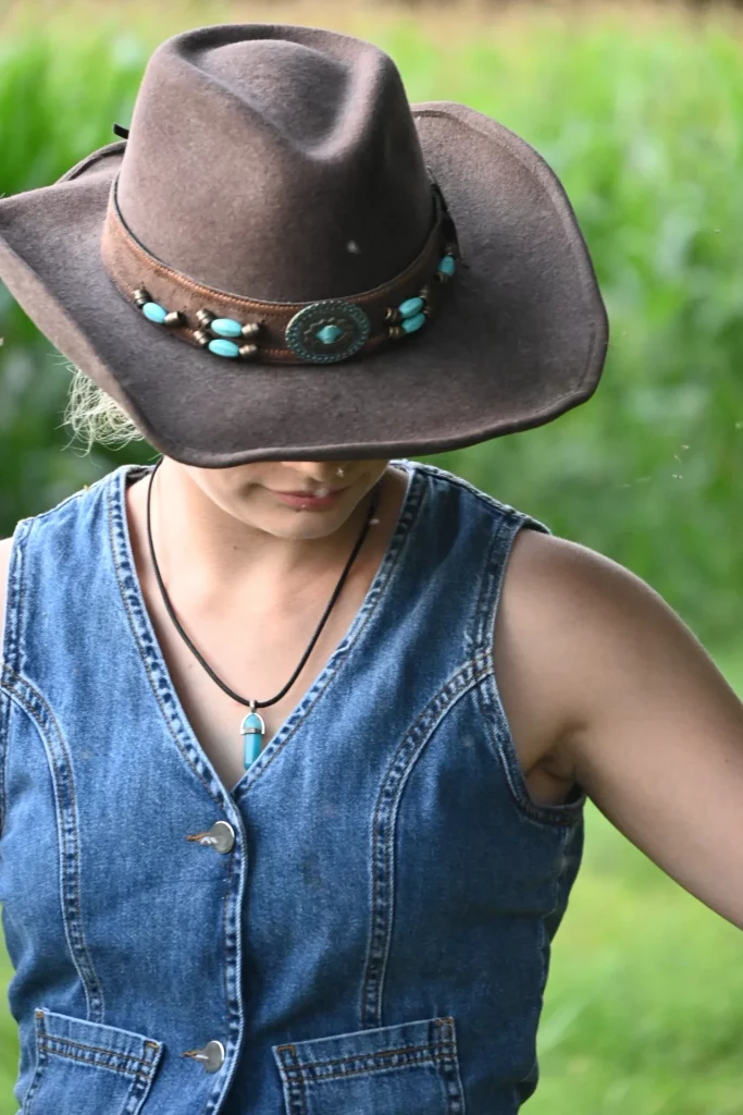 Femme coiffée d'un chapeau de cow-boy orné de pierres turquoise, vêtue d'un gilet en jean et d'un pendentif turquoise.