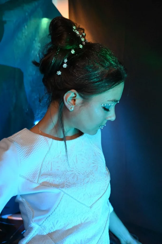 Une femme vêtue d'une robe blanche regarde vers le bas, ses cheveux en chignon orné de petites fleurs blanches.