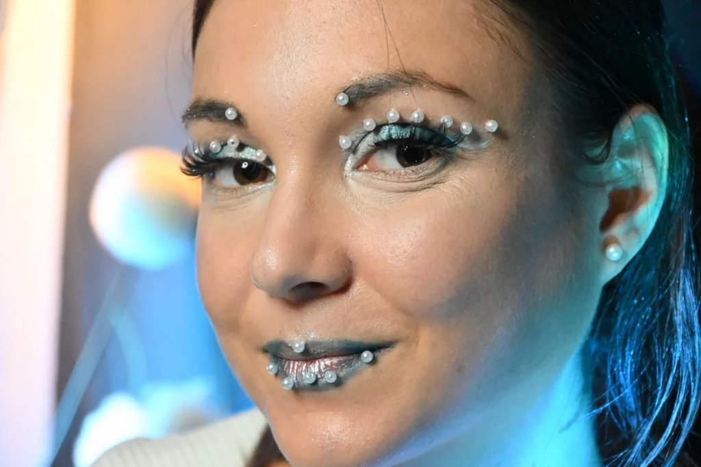 Femme au maquillage artistique, avec des ornements en perles autour des yeux et des lèvres.