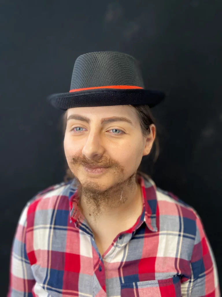 Modèle avec un chapeau et un maquillage SFX de transformation masculine de pose de fausse barbe