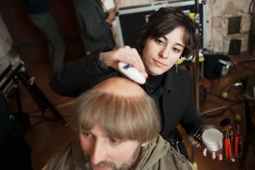 Math David Makeup poudrant le haut du crâne d'un acteur sur le tournage scriptionary à Strasbourg.