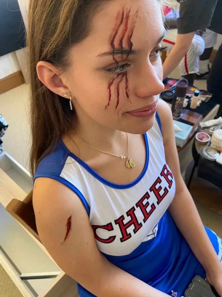 Modèle en tenue de cheerleading avec de fausses marques de griffes en sang sur le visage