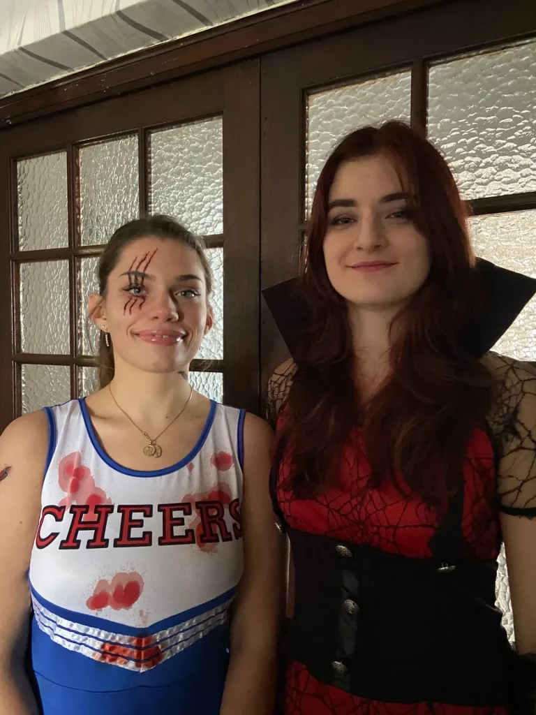 Une pom-pom girl effrayante avec le visage peint et une deuxième personne déguisée en vampire devant une porte