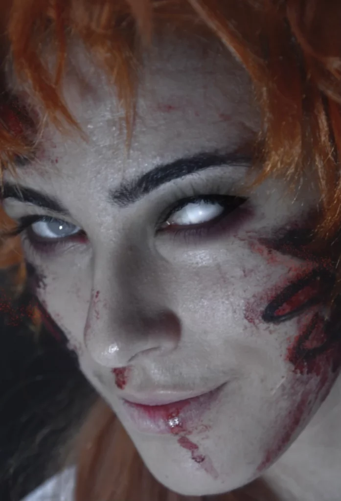Modèle aux yeux blancs intenses et aux cheveux orange. Son visage est maculé de faux sang.