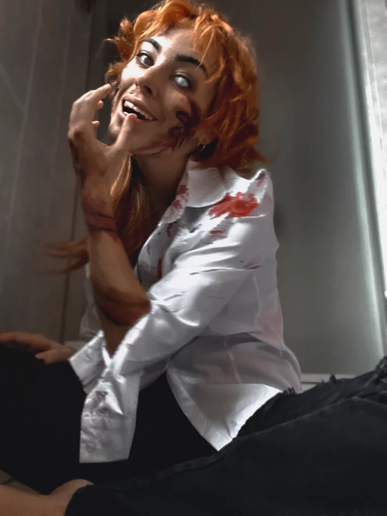 Modèle aux cheveux orange et au sourire sinistre est assise par terre, vêtue d'une chemise blanche tachée de sang