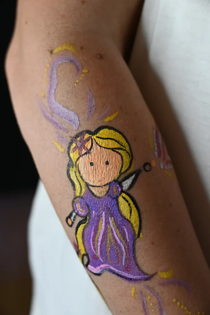 Bras d'un enfant peint d'un visage représentant une princesse de dessin animé, vêtue d'une robe violette et cheveux blonds.
