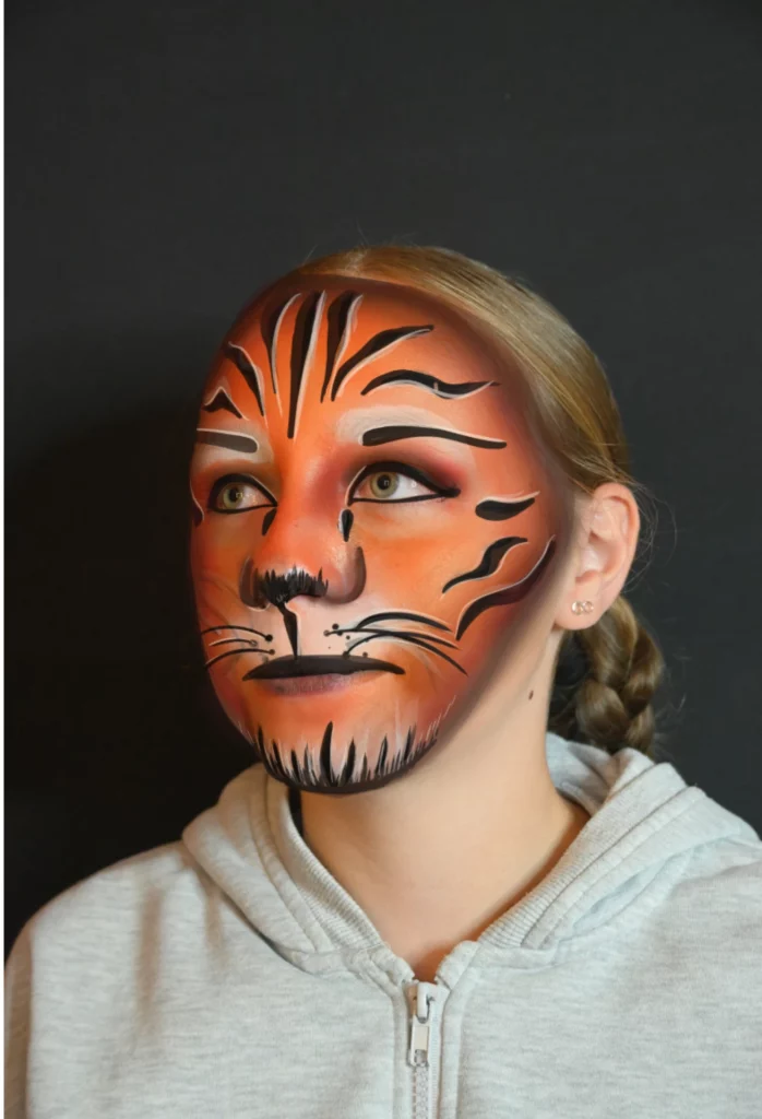 Enfant au visage peint comme un tigre, avec des rayures orange et noires et des yeux expressifs.