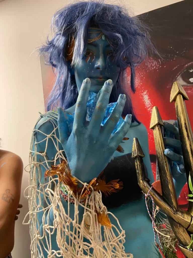 Photo en contre-plongée d'une jeune femme avec la peau bleu portant un filet et un trident.