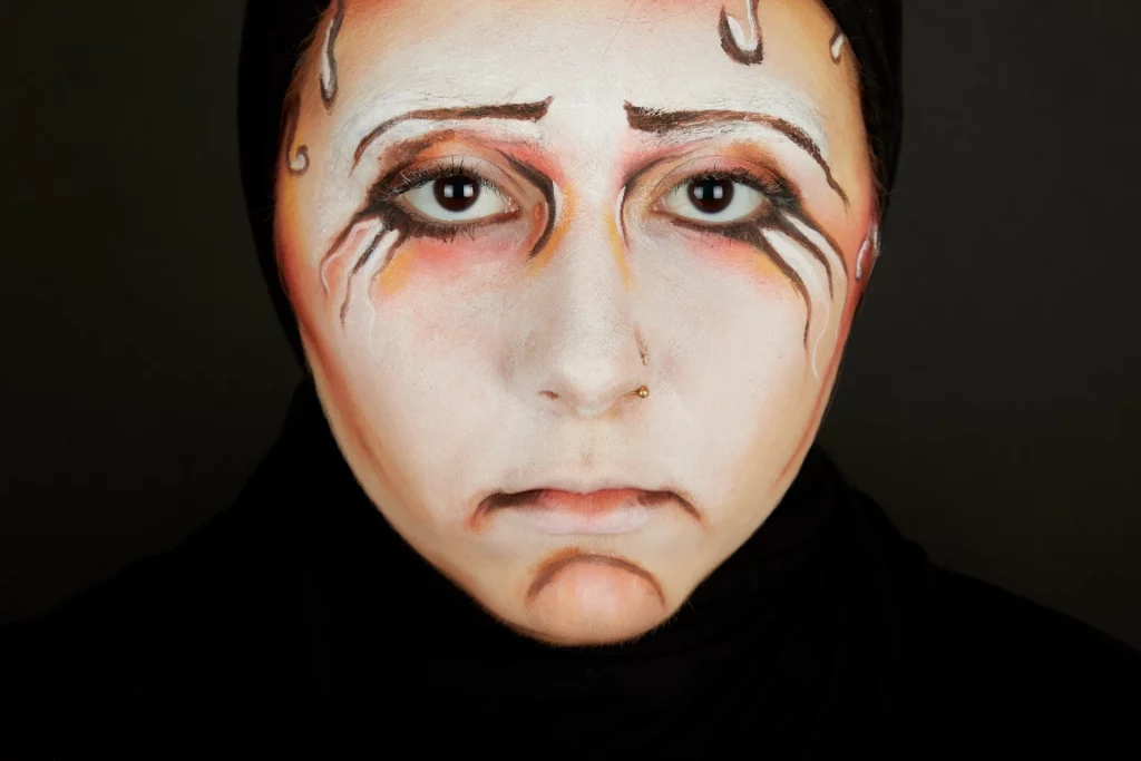 Une personne au maquillage expressif avec un visage solennel sur fond noir.