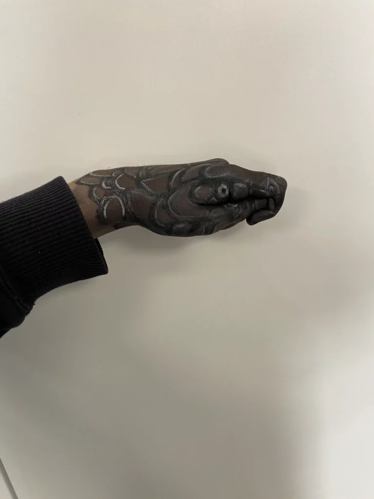 Une main peinte pour ressembler à une tête de serpent, avec des écailles et des yeux détaillés.