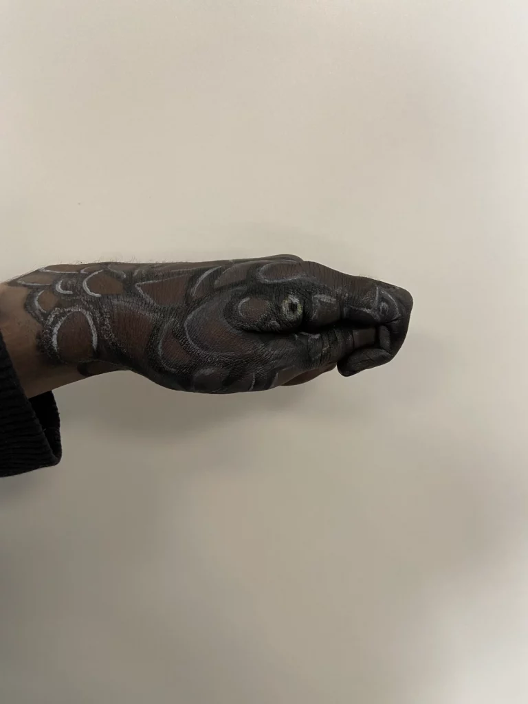 Une main avec un maquillage trompe-l'oeil de tête de serpent, avec des écailles et des yeux détaillés.