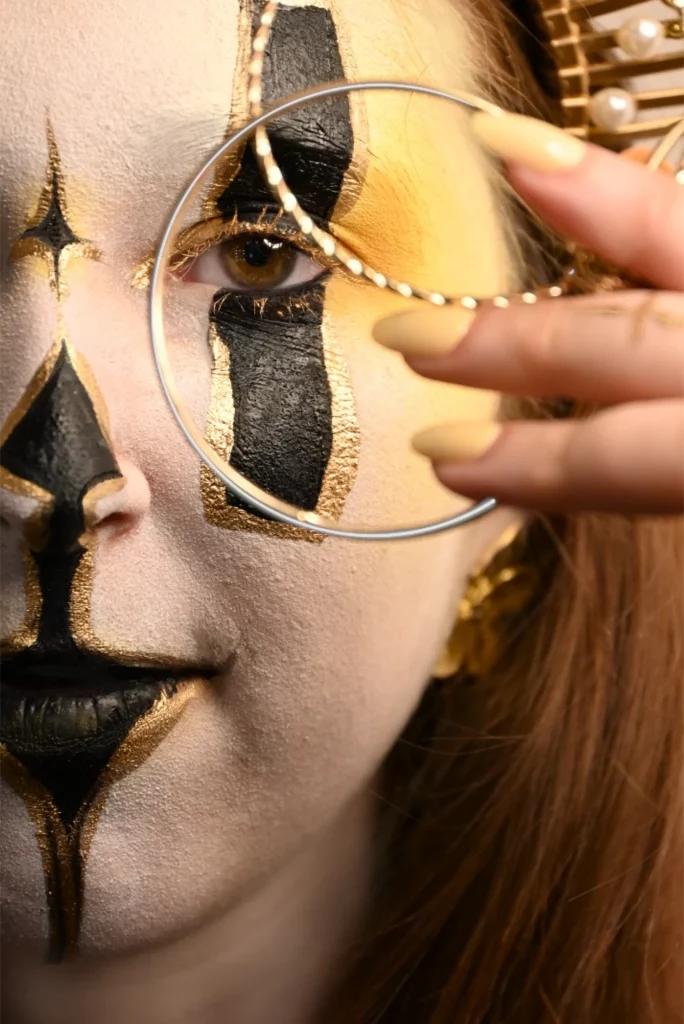 Gros plan du visage avec un maquillage de facepaiting en blanc et doré 2 anneaux doré devant les yeux