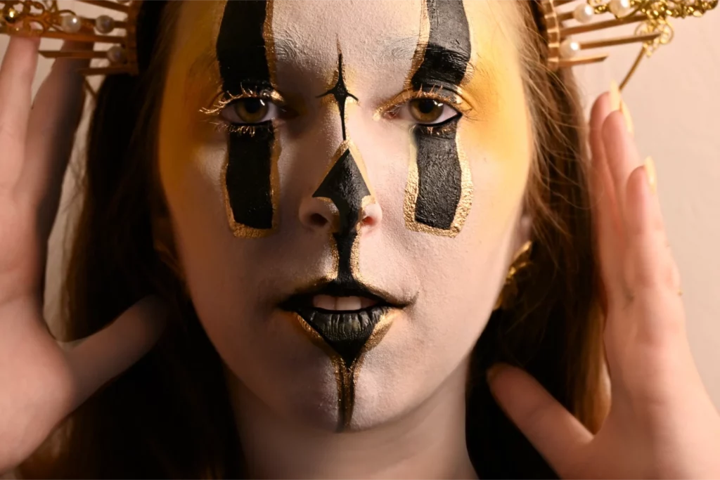 Gros plan du visage avec un maquillage de facepaiting en blanc et doré yeux recouvert de rectangle noir