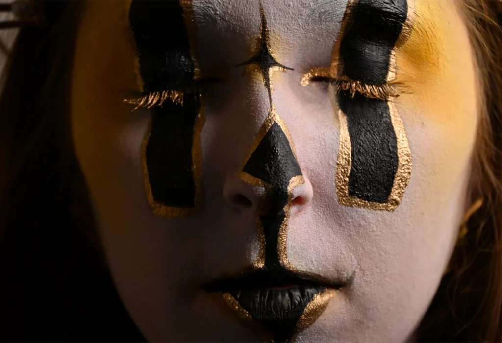 Gros plan visage maquillée de blanc et de dorée yeux fermés recouvert de noirs en forme de rectangle